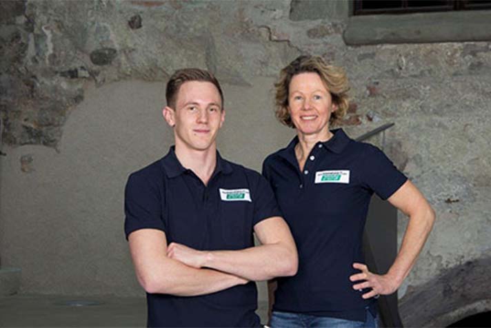 Zwei Mitarbeitende der Kleingkeit GmbH stehen nebeneinander vor einer Steinwand und lächeln